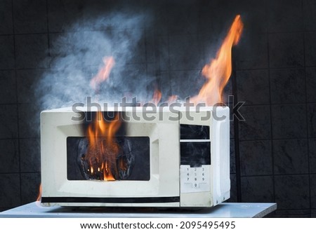 Microwave oven white, in fire front view, electrical appliances caught fire as a result of improper operation Royalty-Free Stock Photo #2095495495