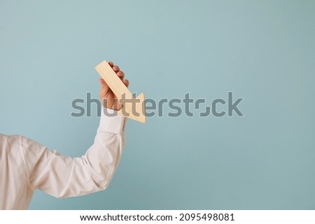 Man holding graph chart arrow that's pointing down on blue blank background with text copyspace. Business problems, profit decrease, lost money, income reduction, financial recession concept Royalty-Free Stock Photo #2095498081