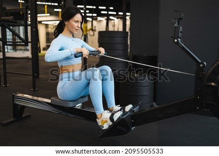 Woman doing exercise on rowing machine in gym Royalty-Free Stock Photo #2095505533