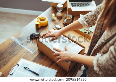 Young woman, owener of small business packing product in boxes, preparing it for delivery. Women packing package with her products that she selling online. Female entrepreneur working at home office  Royalty-Free Stock Photo #2095514530