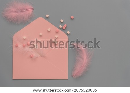 Delicate shades to create a valentine. Pastel colors, top view. Pink envelope, feathers and hearts on a gray background. There's room for text. Invitation to a wedding, birthday or valentine.