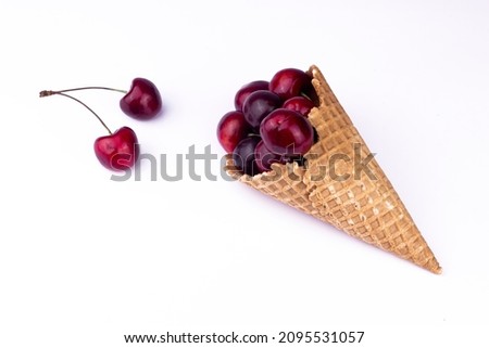 Fresh red cherries in waffle cone. Ice cream cone with ripe sweet cherry on white background with copy space. Summer creative concept flat lay. Top view.