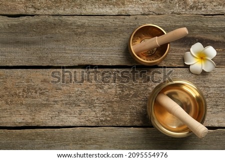 Golden singing bowls, mallets and flower on wooden table, flat lay. Space for text