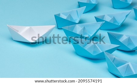 Group of blue paper boats follow white against a light blue background. Strong leader concept, mass manipulation. Starting a business with a well-coordinated team, start-up