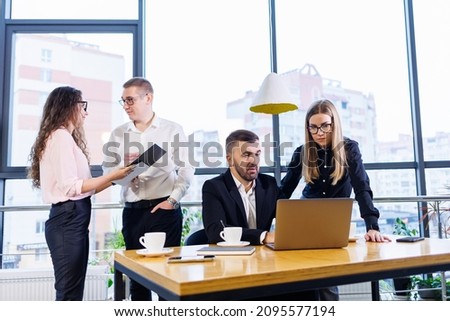 Happy business people looking at laptop presentation, success at work, sitting in modern office. Successful online negotiations. Businessmen share their knowledge