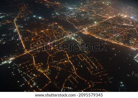 Aerial view from airplane window of buildings and bright illuminated streets in city residential area at night. Dark urban landscape at high altitude Royalty-Free Stock Photo #2095579345