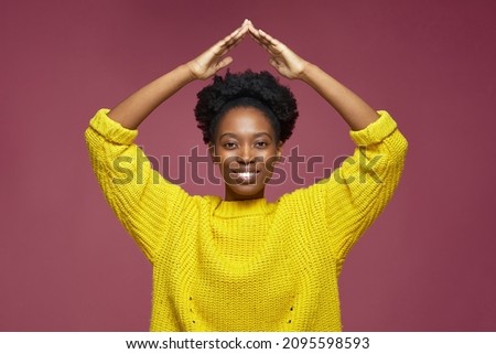 Happy young african american woman with afro hair make home roof gesture by hands over head. Mortgage insurance concept