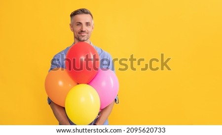 smiling handsome man hold party balloons on yellow background, copy space, shopping