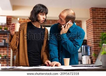 Manager talking on phone with businessman discussing marketing strategy while working at company presentation with entrepreneur woman in startup office. Businesspeople analyzing business document