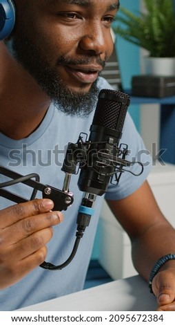 Close up of vlogger using microphone and headphones to record vlog for channel. Positive man with modern equipment filming video for social media podcast. Blogger recording in studio