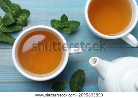 Hot aromatic mint tea on light blue wooden table, flat lay