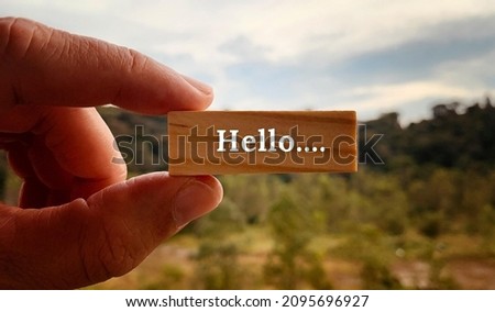 Image with Hello text on a wooden block with a hand holding with and blurred nature background