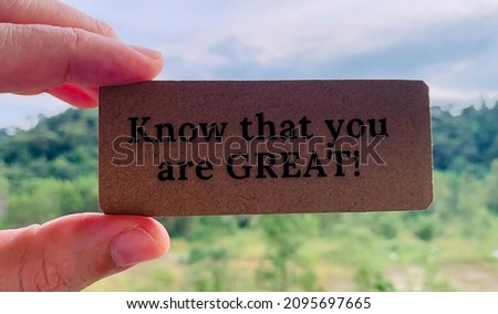 Image with text saying know that you are great written on a brown small cardboard with blurred nature background. Close up