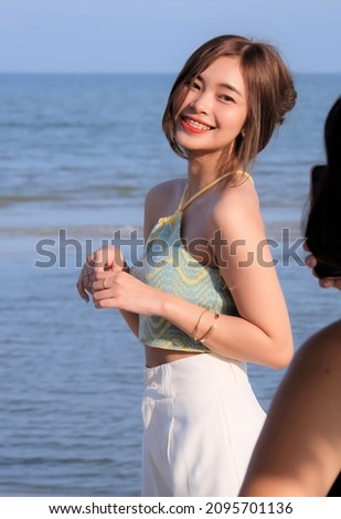 A beautiful girl poses for her friend to take a photo. At the beach by the sea.