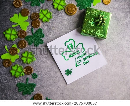 Decorative clover leaves, green gifts box, coins on stone background, flat lay. St. Patrick's Day celebration with  card Happy Saint Patricks Day