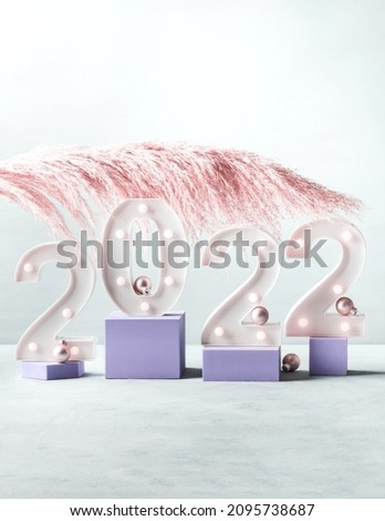 New year 2022 lights numbers with pink pampas branch and golden decor on purple color geometric podiums. Minimal celebrating new year scene
