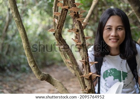 A woman doing a forest planting activity takes pictures with mushrooms growing in the trees.