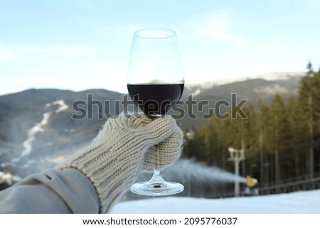 Hand in mitten holds glass of wine against mountains