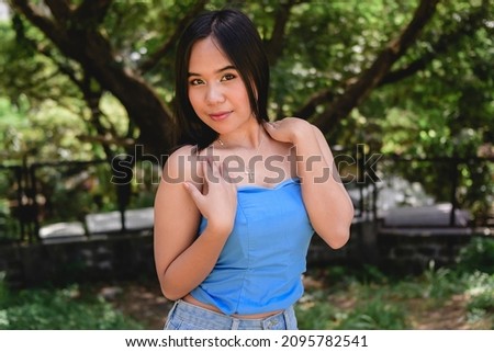 A pretty and attractive southeast asian woman in a powder blue tube top. Outdoor nature park scene.
