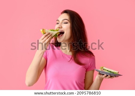 Young woman eating tasty sandwich on color background Royalty-Free Stock Photo #2095786810