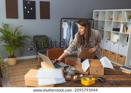 Working woman at online shop. She is wearing casual clothing and packaging goods for delivery. Women, owener of small business packing product in boxes, preparing it for delivery