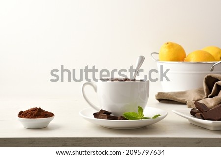Hot chocolate in white ceramic mug, pieces and chocolate powder in bowl on wooden table white isolated background. Front view. Horizontal composition.