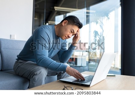 Pensive asian man working in office on laptop, anxious business man in modern office, frustrated depressed Royalty-Free Stock Photo #2095803844