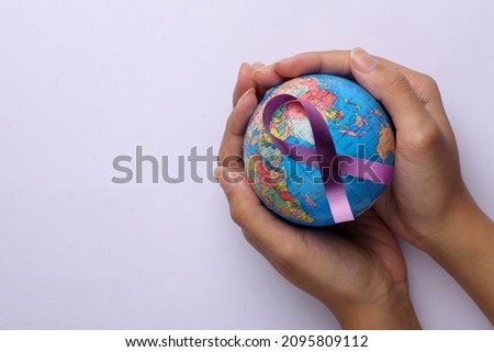 Hands holding a globe with purple ribbon for cancer awareness