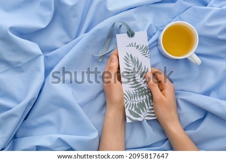Woman with bookmark and cup of tea on bed