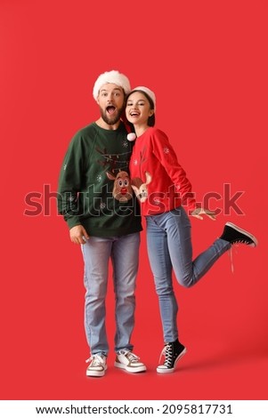 Happy young couple in stylish Christmas clothes on color background
