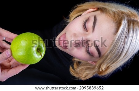 Blondes in black T-shirts on a black background. Eat a green apple. A bone of contention is the core, or the core of the dispute, or a small issue that can lead to a larger dispute.