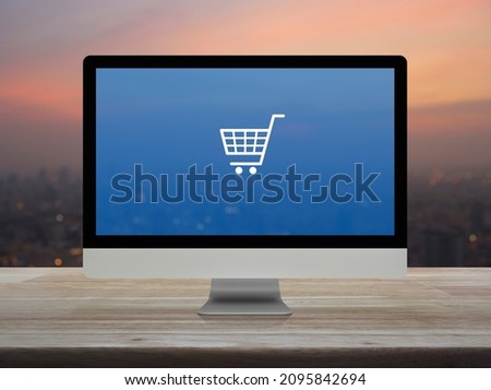 Shopping cart flat icon on desktop modern computer monitor screen on wooden table over blur of cityscape on warm light sundown, Business shop online concept