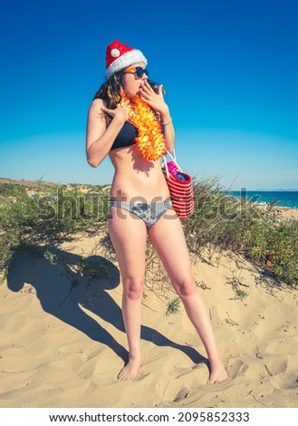 Young brunette woman in a Santa Claus hat and bikini in the shock of what she saw against the backdrop of the sea coast
