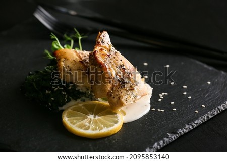 Board with baked cod fillet, pesto sauce and lemon on table in restaurant