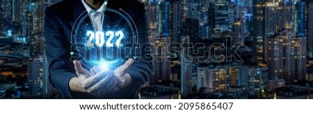Businessman holding 2022 virtual number with big city night background and copy space for merry christmas and happy new year concept. 