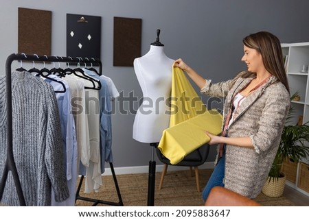 Young female dressmaker choosing material from catalogue in studio. Tailor looking through fabrics while standing in a sewing workshop. Young clothing designer holding fabric samples