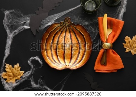 Pumpkin shaped plate, cutlery, napkin and Halloween decor on black background