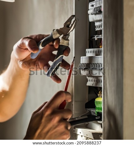 Man, an electrical technician working in a switchboard with fuses. Installation and connection of electrical equipment. Professional with tools in hand. concept of complex work, space for text. Royalty-Free Stock Photo #2095888237
