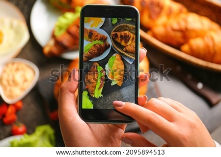 Woman taking a picture of tasty croissant sandwiches at kitchen table