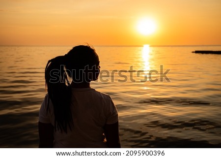 Woman Looking at the Sunset by the Sea. Silhouette of a dreamer girl looking hopeful at the horizon.