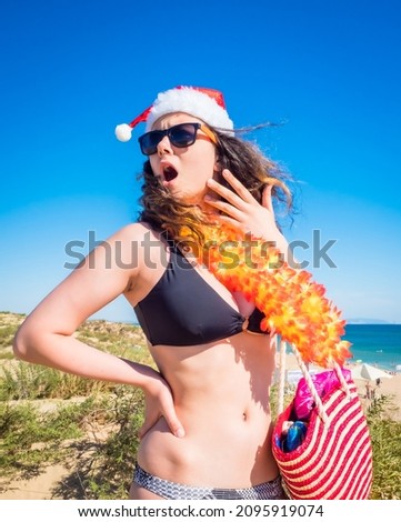 Young brunette woman in a Santa Claus hat and bikini in the shock of what she saw against the backdrop of the sea coast