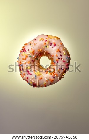 A vertical shot of a donut with white frosting and rainbow sprinkles on a yellow background