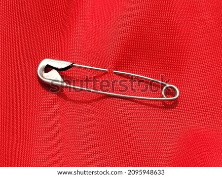 Safety pin attached to red shirt background Royalty-Free Stock Photo #2095948633