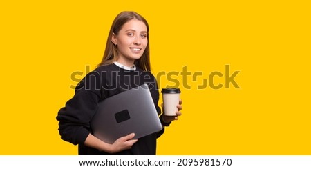 Photo of beautiful girl carrying laptop and hold a cup of coffee over yellow background