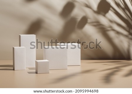 Abstract minimal nature scene - empty stage with five white rectangle podiums on beige background and shadows of tree leaves. Pedestal for cosmetic product and packaging mockups display presentation
