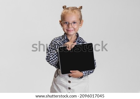 Teleworking. Cute little girl with tablet isolated over gray background. Boss kid. Model wearing checkered shirt and glasses. Concept of childhood, education, motherhood. Copy space for ad