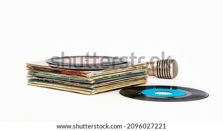 A stack of old vinyl records and a microphone for karaoke on a white background.