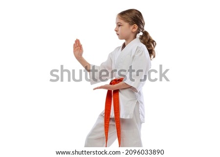 Punch forward. Portrait of little girl, young karate in white kimono, judoji training alone isolated over white background. Concept of sport, education, skills, workout, healthy lifestyle and ad