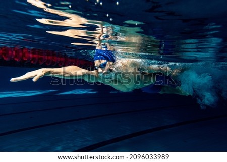 Preparing to competition. Professional male swimmer in swimming cap and goggles in motion and action during training at pool, indoors. Healthy lifestyle, power, energy, sports movement concept Royalty-Free Stock Photo #2096033989