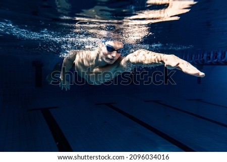 Close-up. Young male swimmer in swimming cap and goggles in motion and action during training at pool, indoors. Underwater imaging. Healthy lifestyle, power, energy, sports movement concept Royalty-Free Stock Photo #2096034016